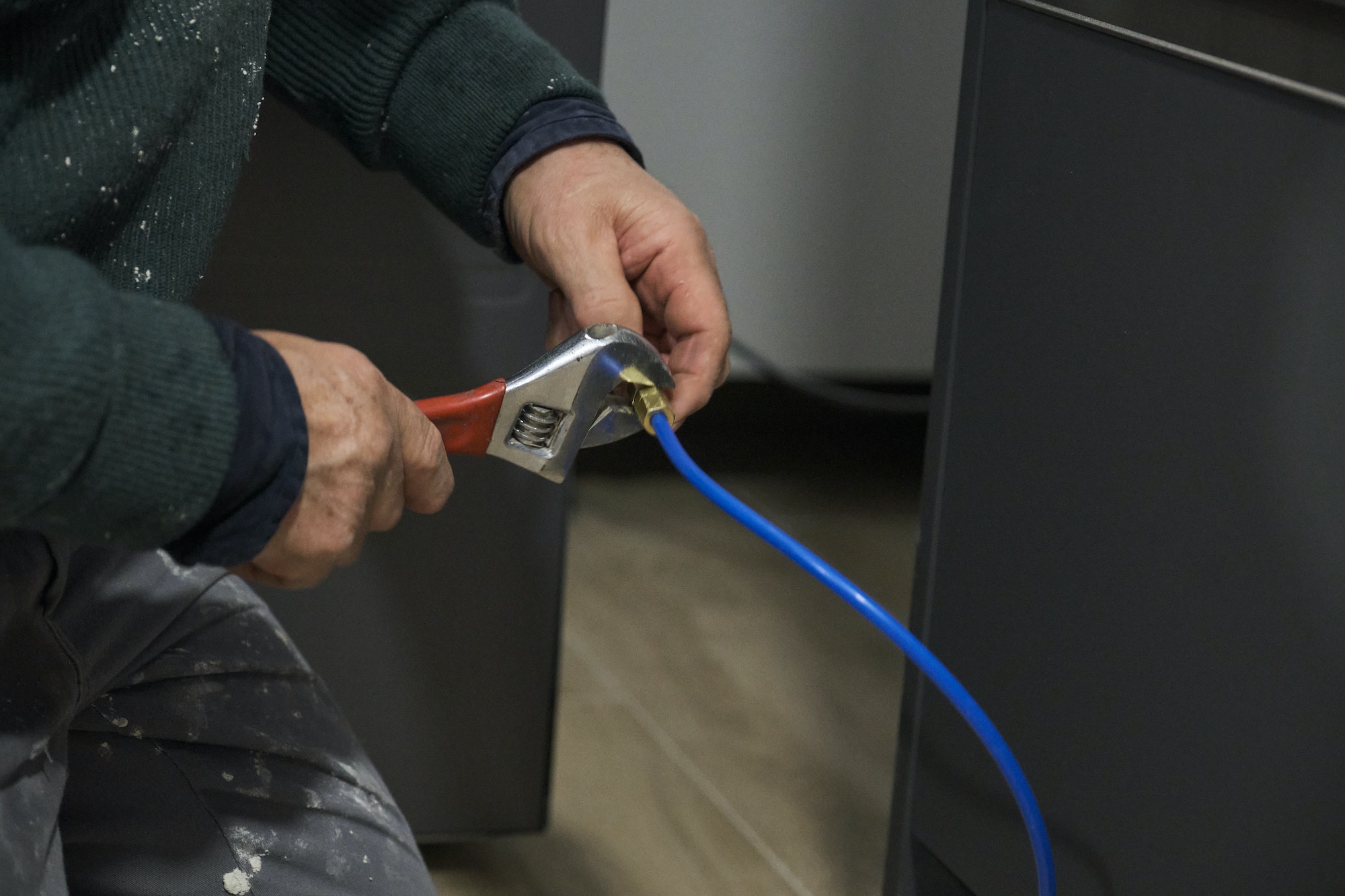 Mature technician hands install water filter use a wrench to an american fridge.